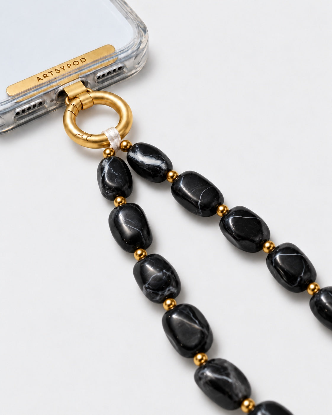 Close-up of ARTSYPOD black marble marbled beaded phone wristlet with gold-tone hardware attached to a clear phone case