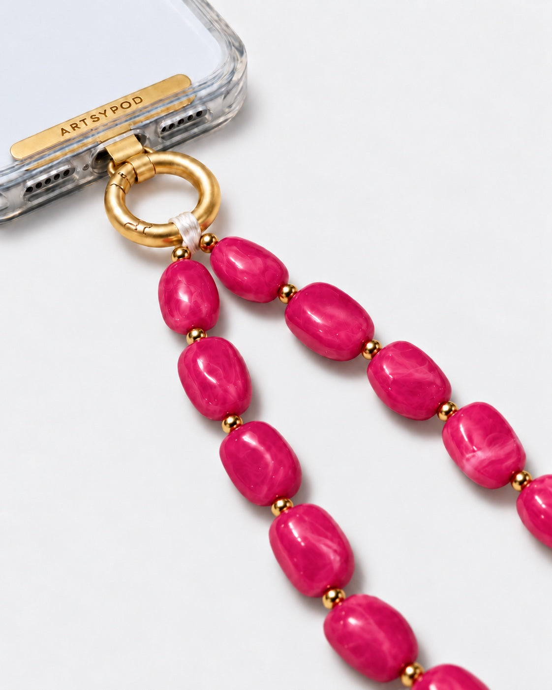 Close-up of ARTSYPOD fuchsia pink marbled beaded phone wristlet with gold-tone hardware attached to a clear phone case