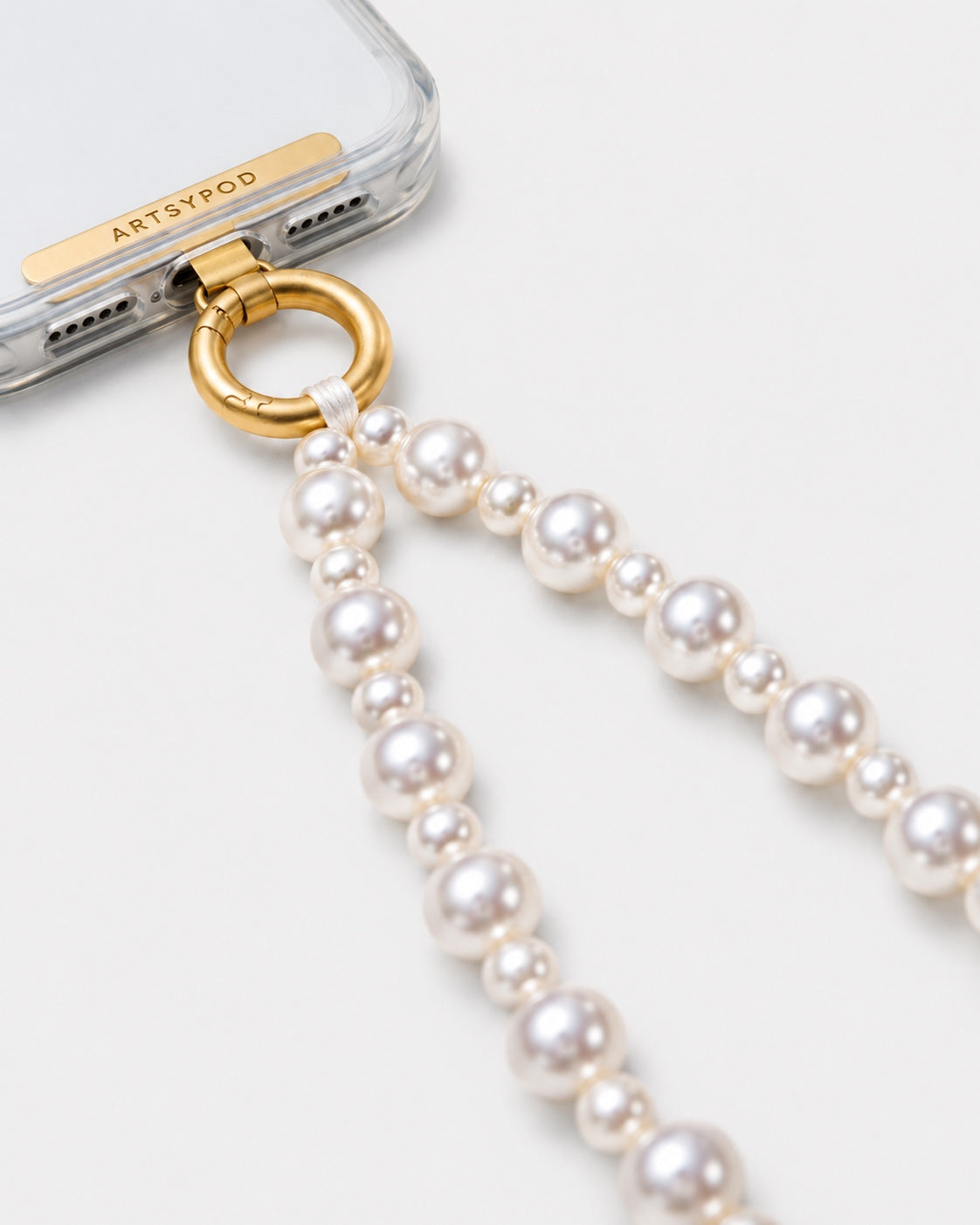 Close up of ARTSYPOD pearl phone wristlet gold ring clasp and tab attached to clear phone case