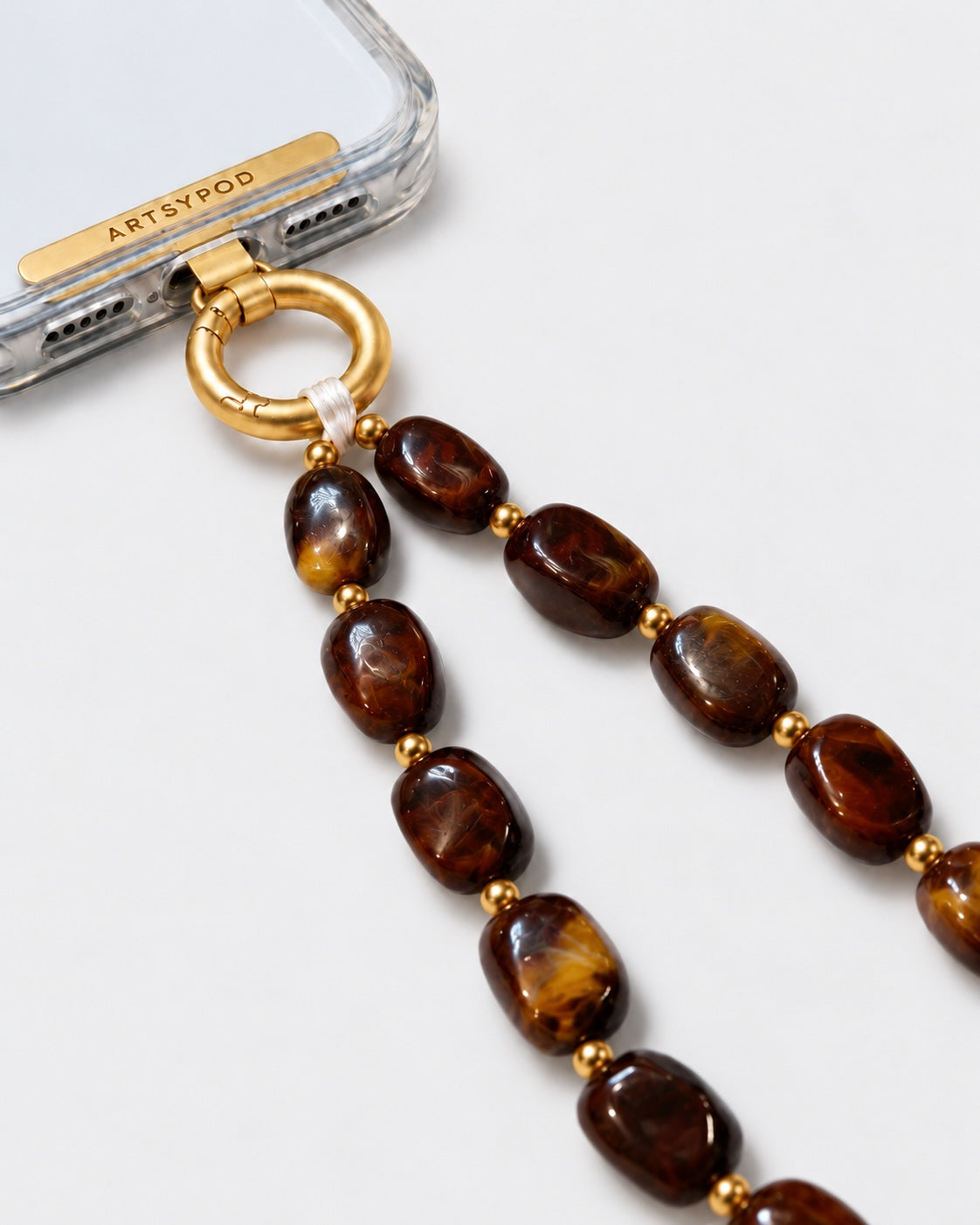 Close-up of ARTSYPOD amber brown marbled beaded phone wristlet with gold-tone hardware attached to a clear phone case